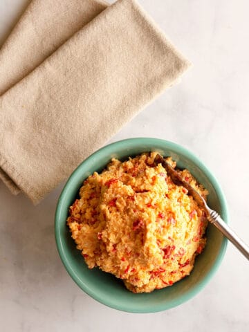 A vintage turquoise bowl of Pimento cheese with a spreader and two napkins beside