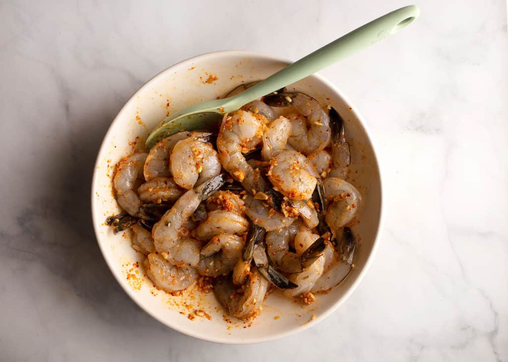 Shrimp coated with marinade ingredients in large bowl