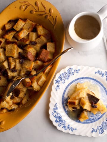 A baking dish with Old-Fashioned Bread Pudding and a serving on a small blue and white plate