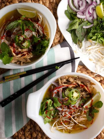 Two bowls of Vietnamese Chicken Pho with condiments and chopsticks
