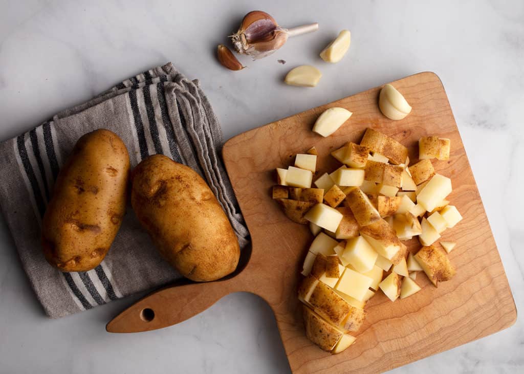Chopped russet potatoes and garlic on a wooden cutting board