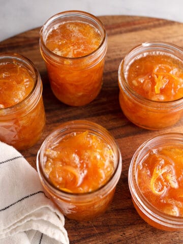 Five jars of homemade orange marmalade on a wooden board