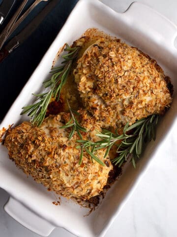Two bone-in chicken breasts in a baking dish garnished with rosemary sprigs