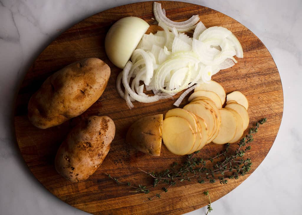Potatoes and onions being thinly cut on a cutting board