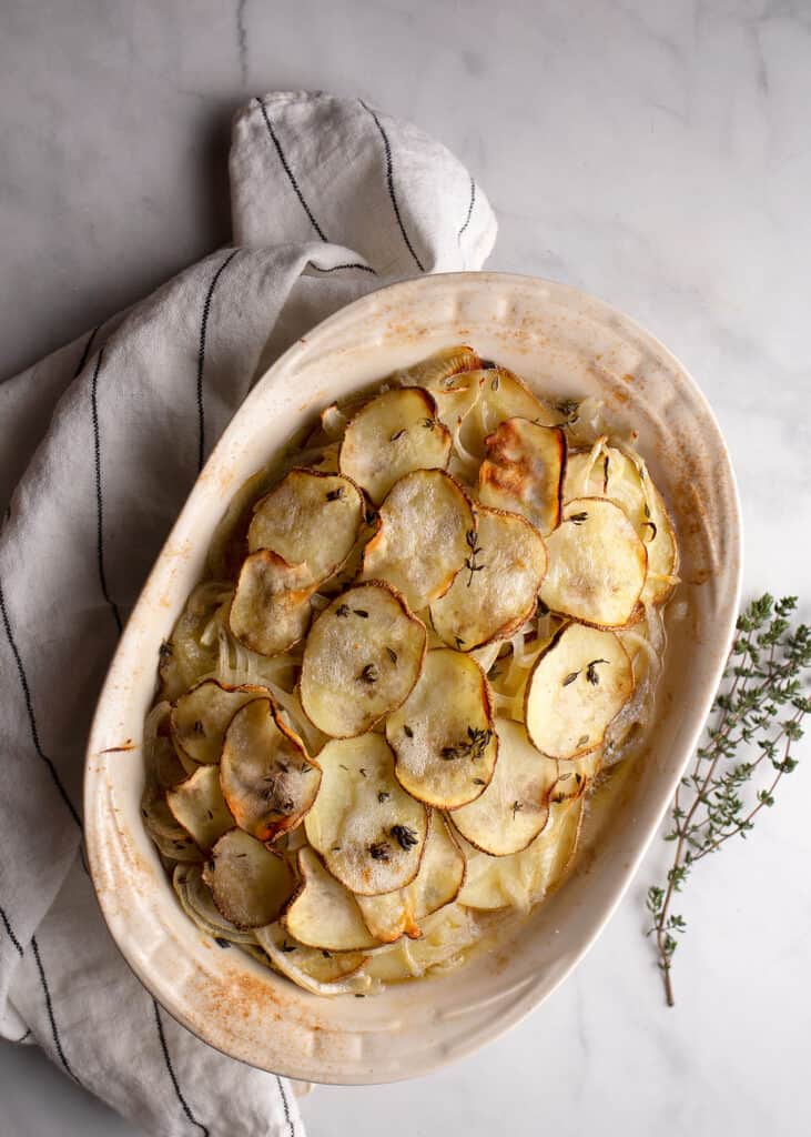Boulangere Potatoes in a baking dish with thyme lying beside