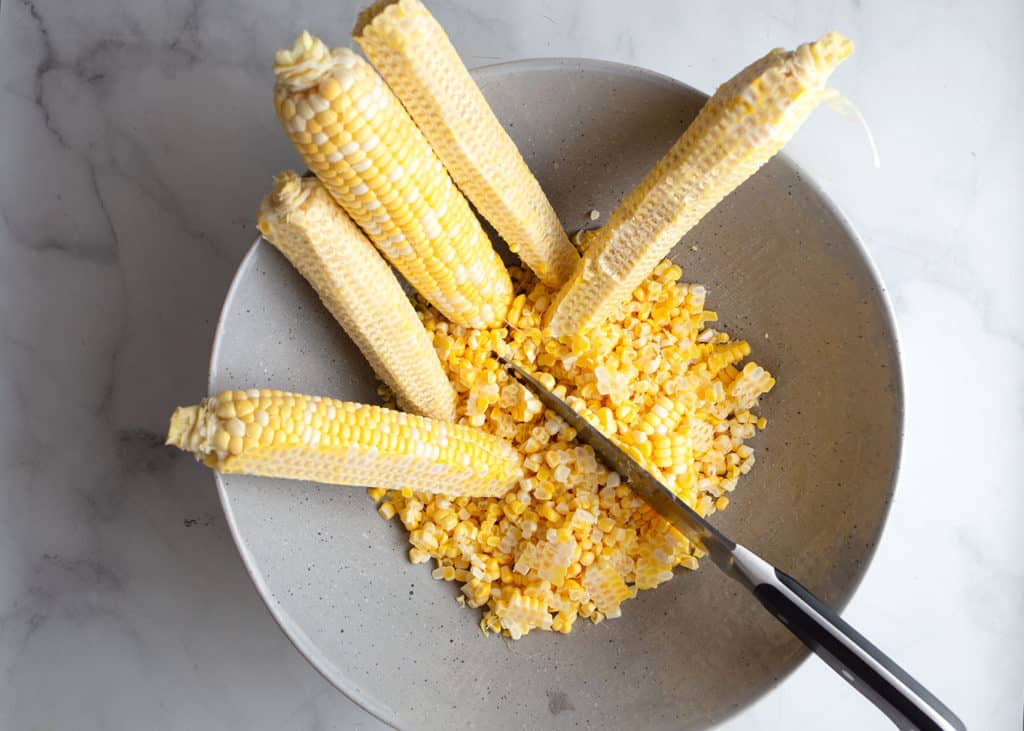 Cutting the kernels off the cob into a large bowl