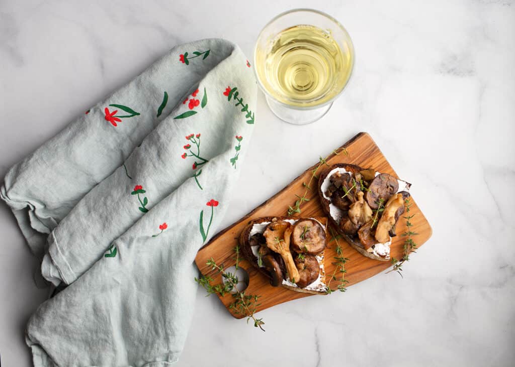 Mushroom Tartines with Goat Cheese on a board with a glass of white wine