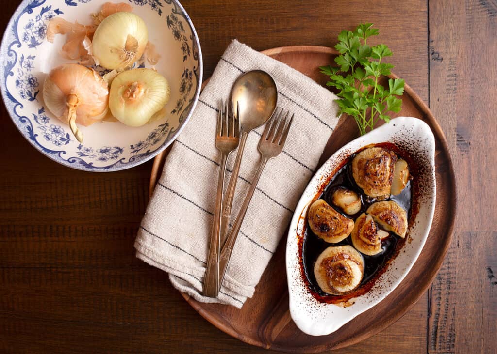 Balsamic Roasted Onions on a wooden tray with vintage silverware on a linen napkin