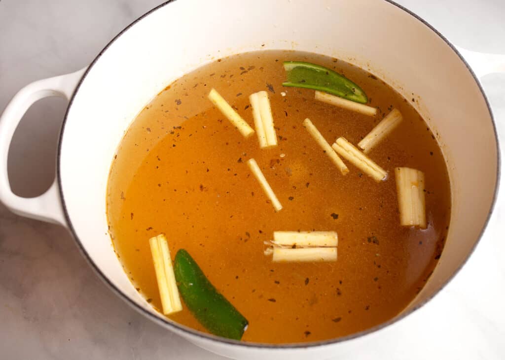 Lemongrass, ginger, and jalapenos in chicken broth in a large pot