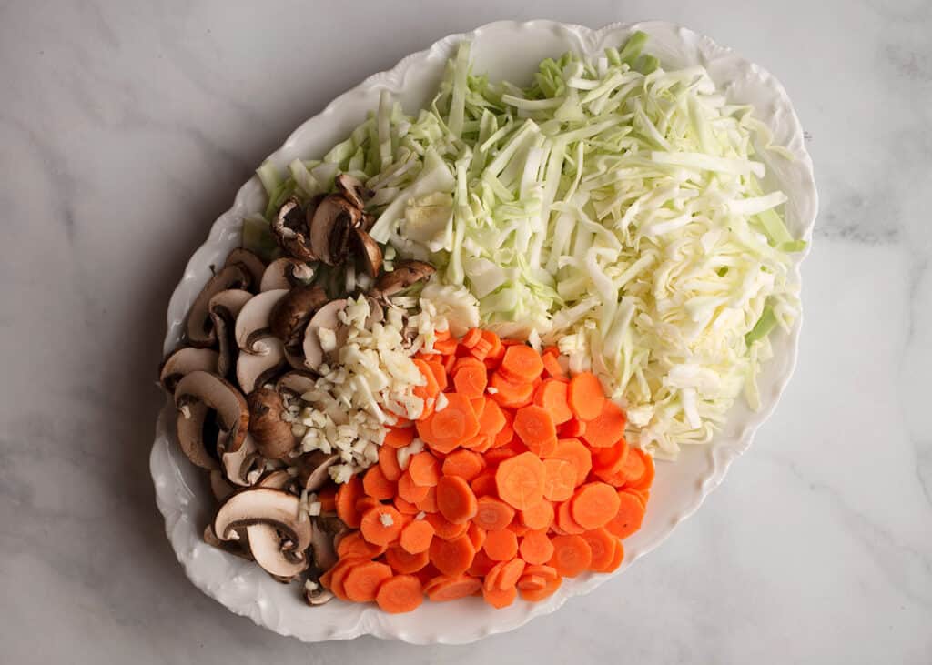 Shredded cabbage, sliced mushrooms and carrots, and chopped garlic on a platter