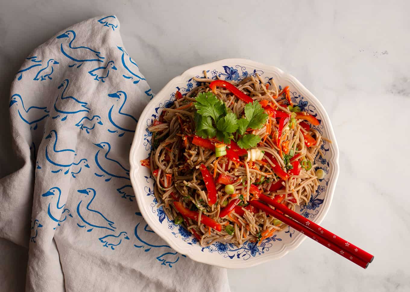 Sesame Noodle Salad in a blue and white bowl with red chopsticks