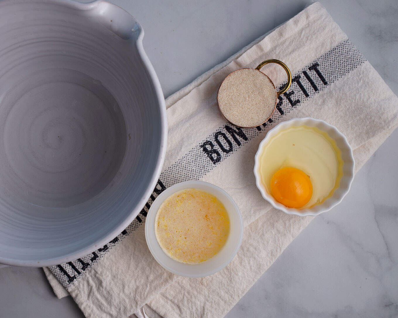A mixing bowl waiting to mix up Apple Fritters. Egg, melted butter, and sugar and measured out beside.