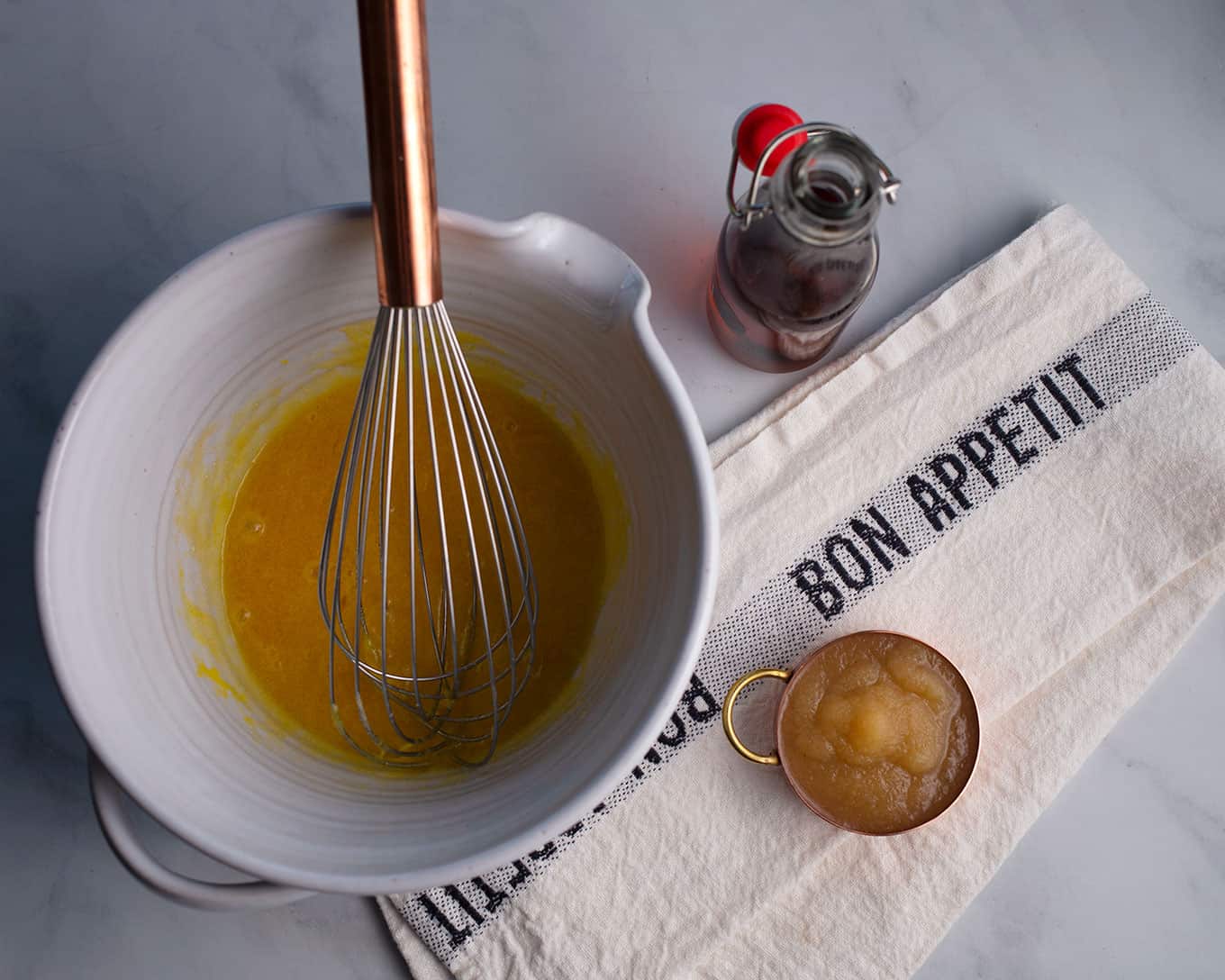 Applesauce is added to the batter along with vanilla flavoring using a whisk.
