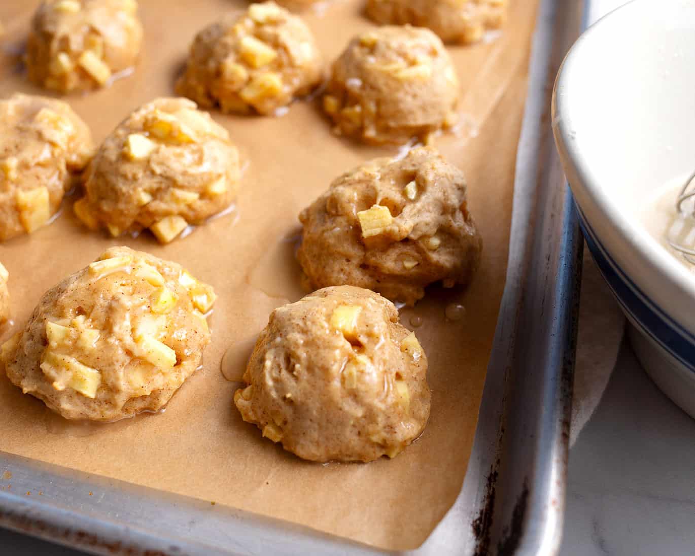 Glazed apple fritters on a parchment lined sheet pan.