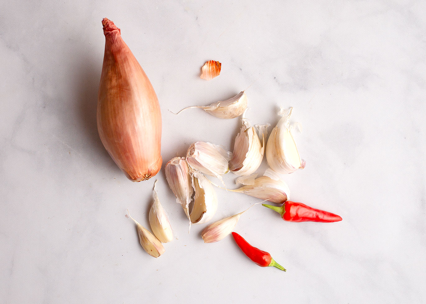 Whole shallot, garlic cloves, and peppers on a marble surface