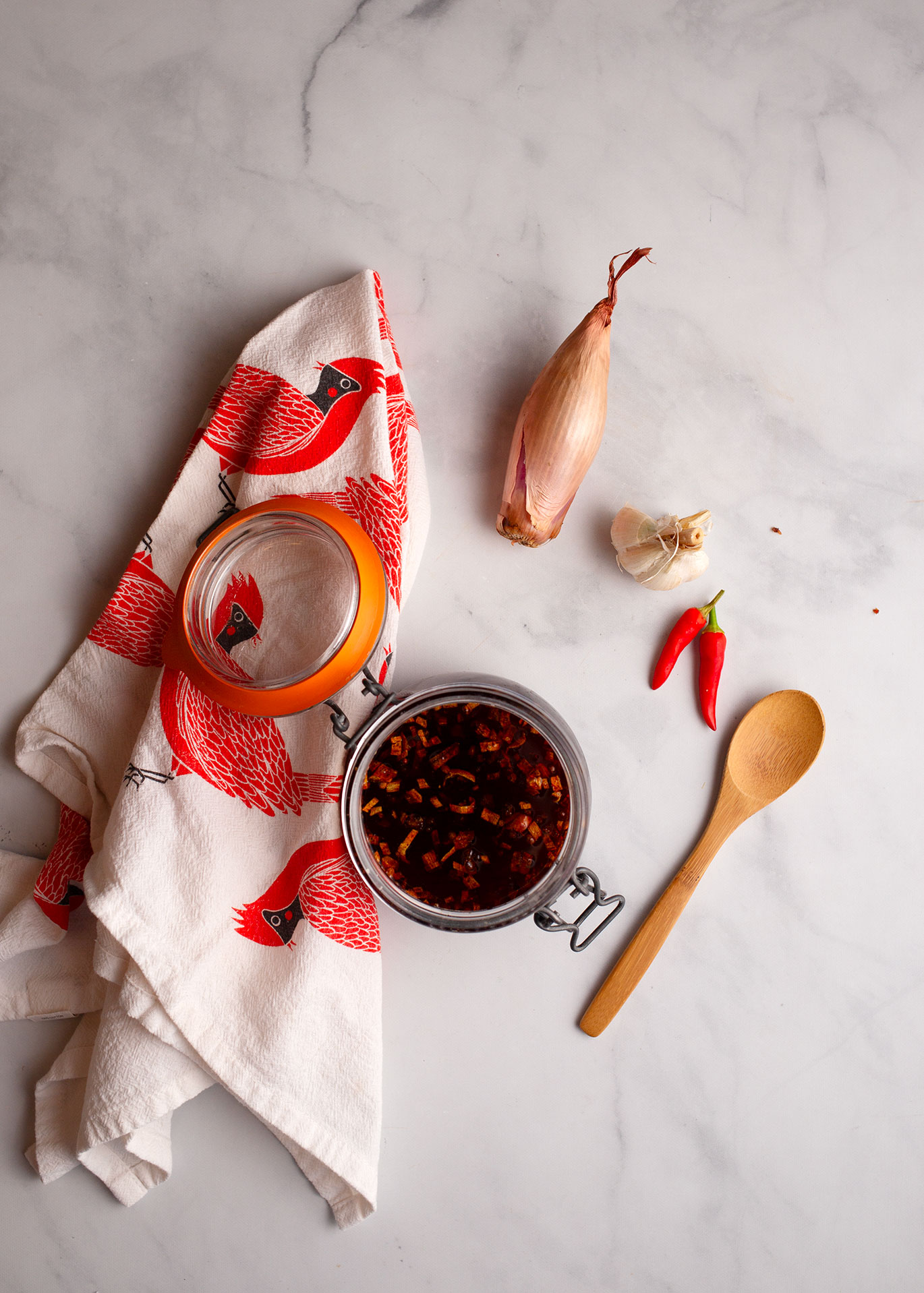 Finished chili crisp in a glass storage jar with small wooden spoon to serve.