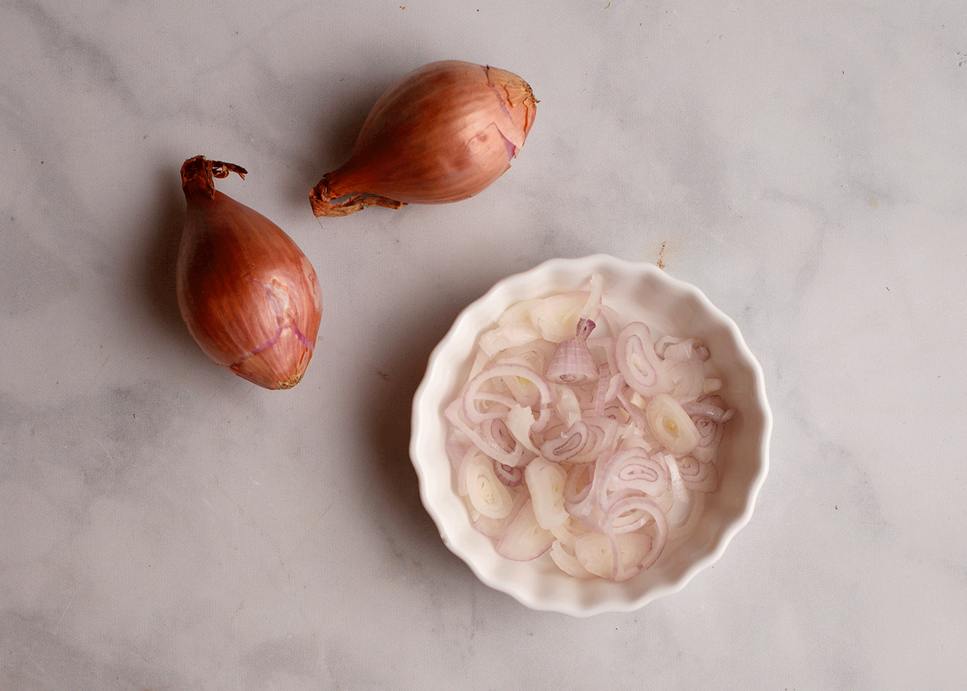 Shallot cut into rings in a small white dish with two shallots laying beside