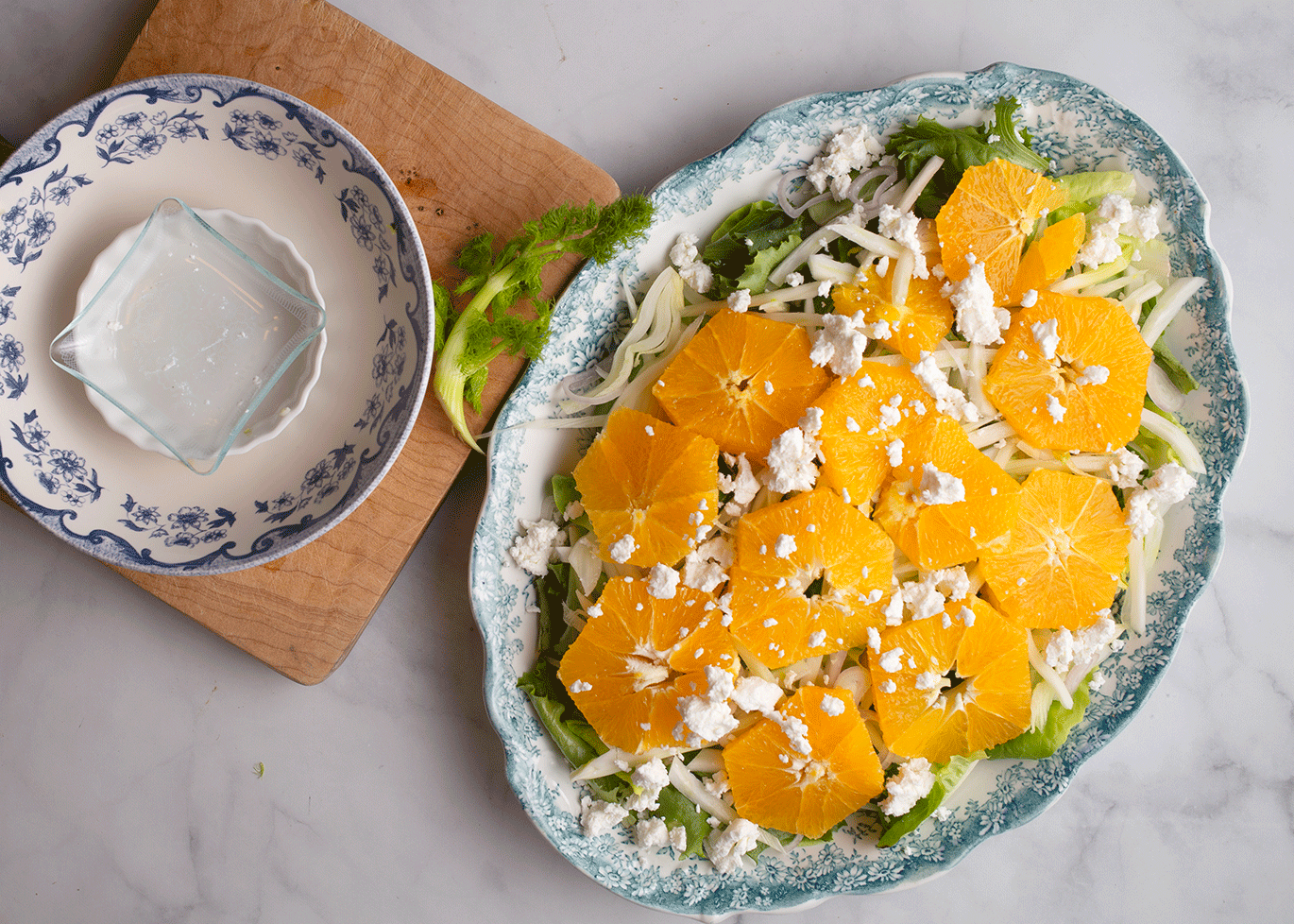 Layer lettuce, fennel, shallot, oranges, and goat cheese on a large platter.