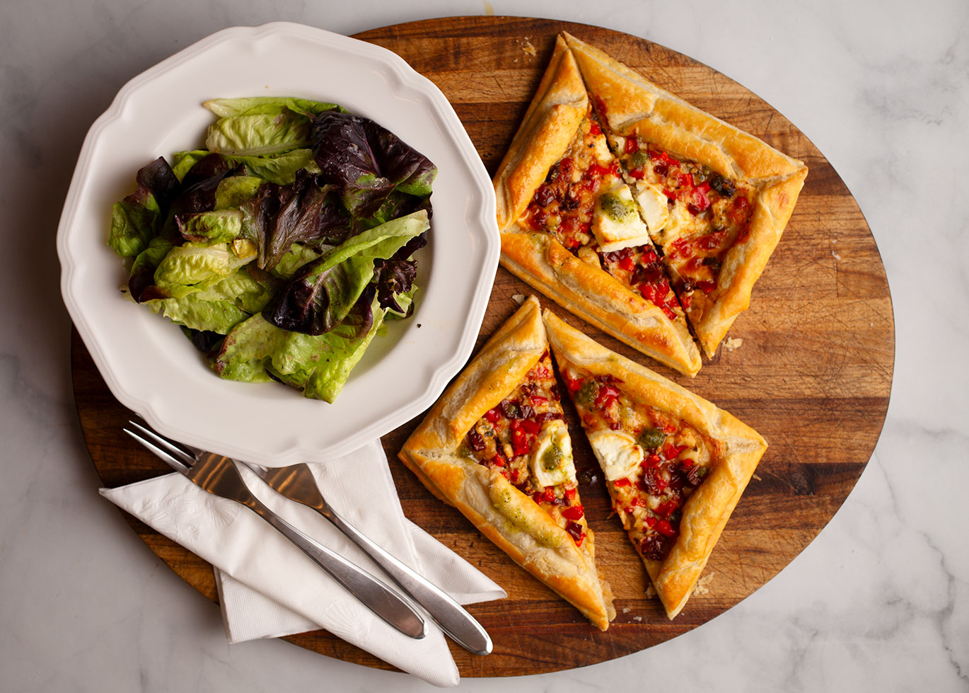 Two 4 Cheese & Sundried Tomato Tarts on a wooden board with a green salad.