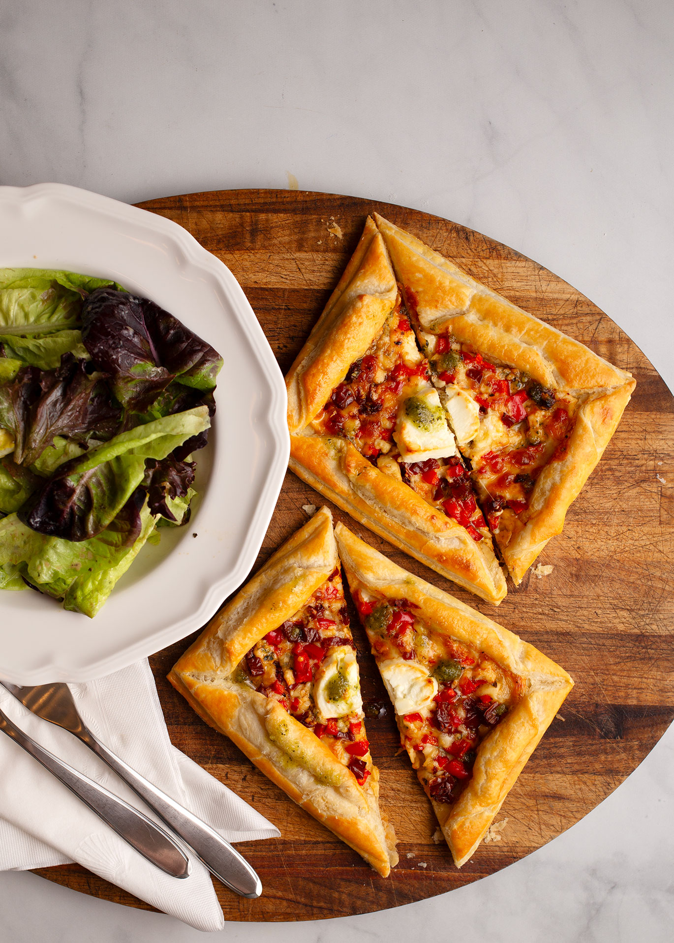 Vertical photo of two 4 Cheese & Sundried Tomato Tarts on a wooden board with a green salad.