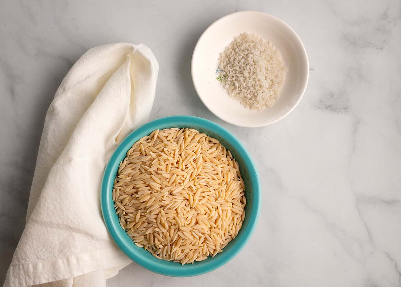 Fresh orzo pasta with salt in a turquoise bowl, ready for cooking or meal preparation.