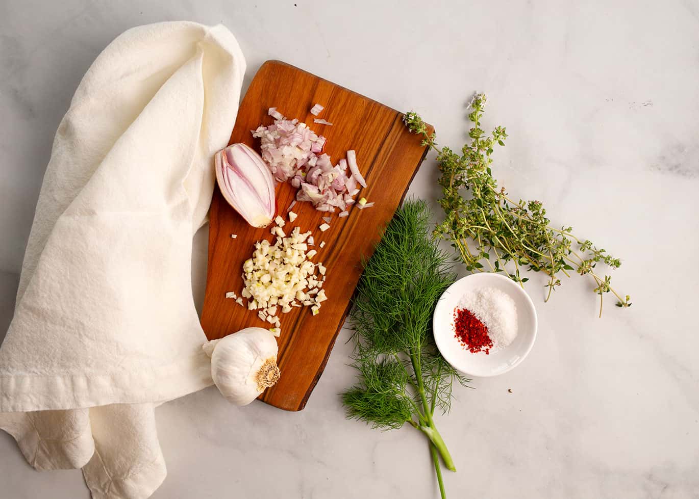 Fresh garlic, chopped shallots, herbs, and spices arranged on a wooden cutting board for vinaigrette
