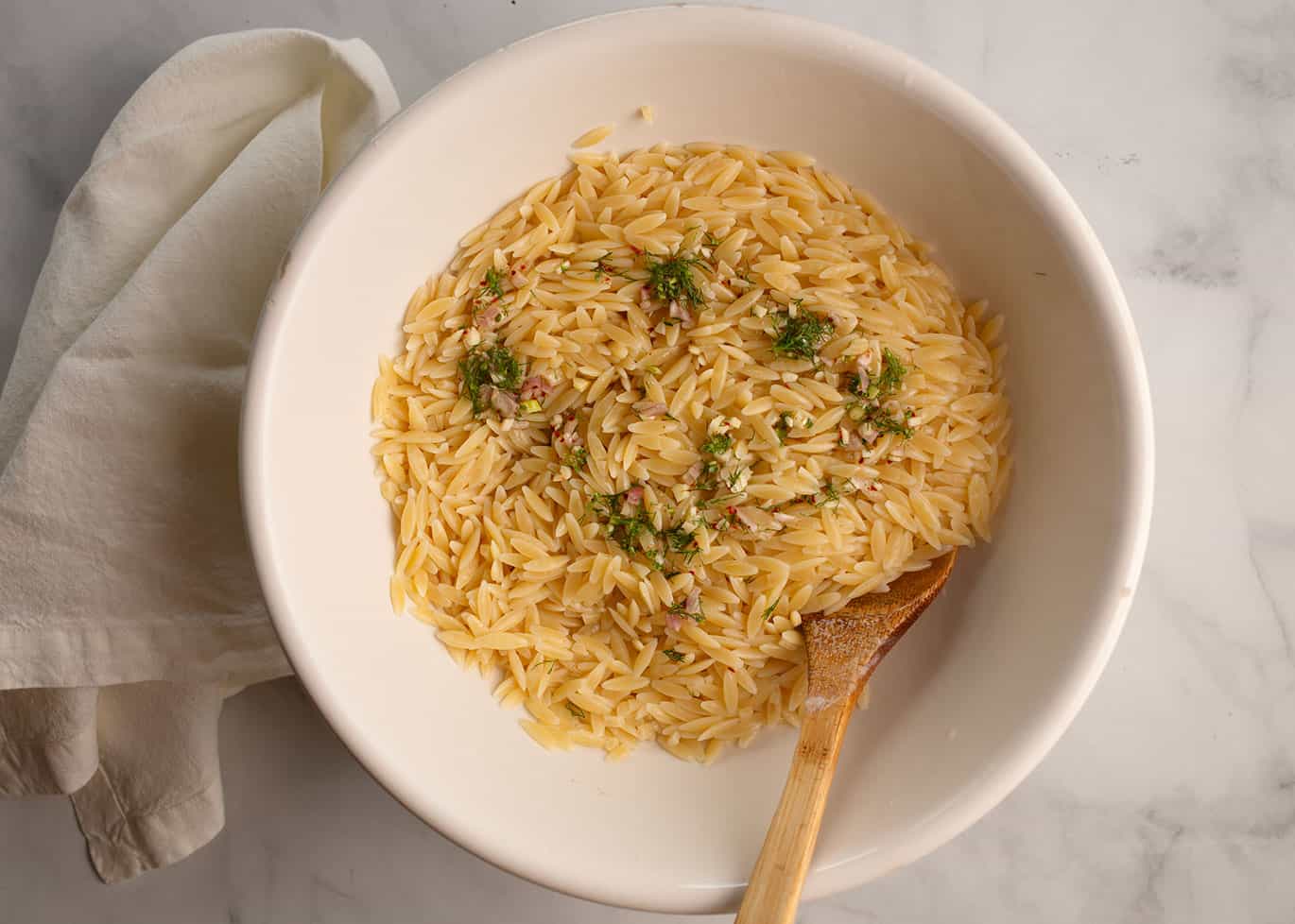 Orzo pasta with herbs in a white bowl.