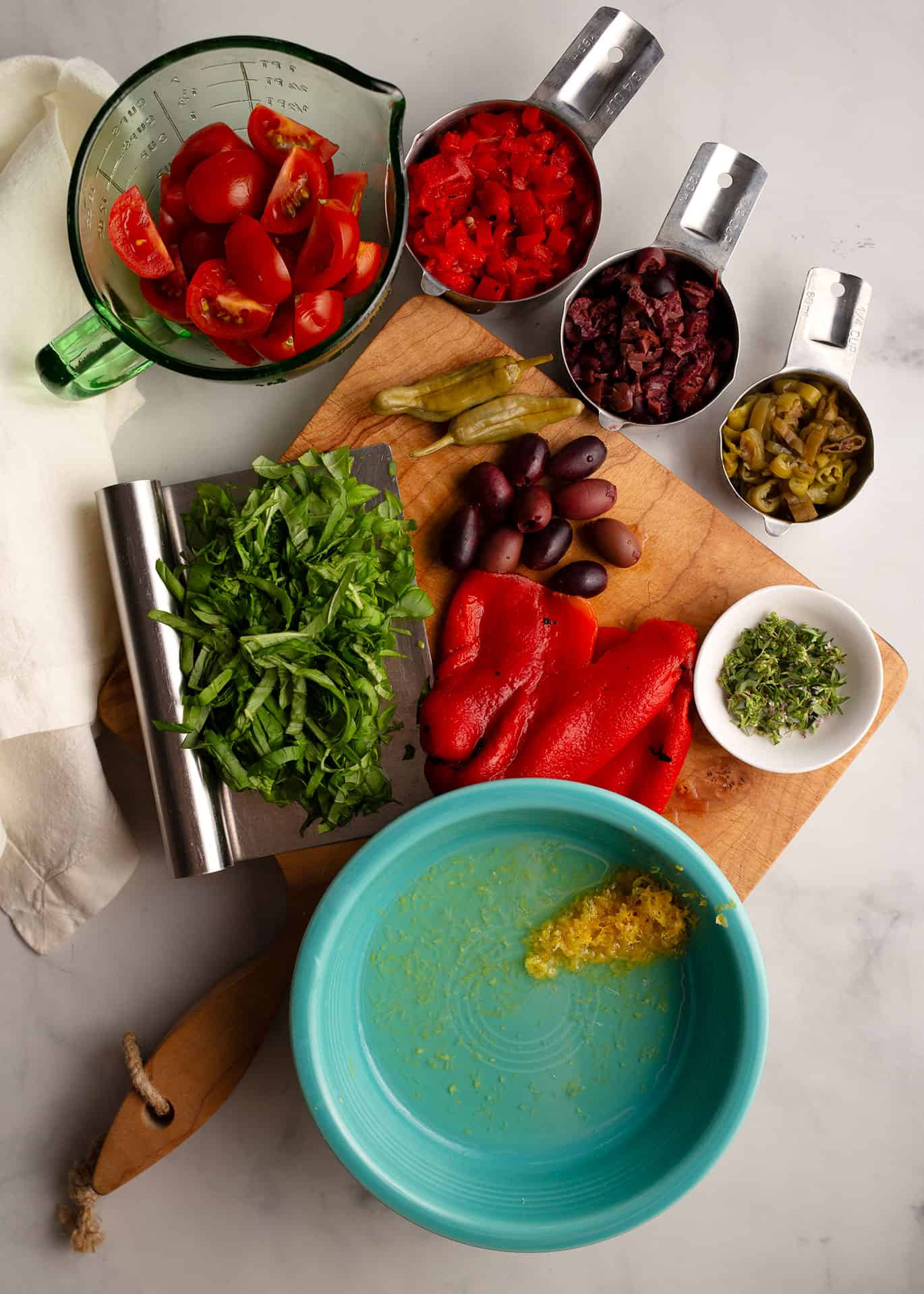 Mediterranean Orzo Salad ingredients include tomatoes, roasted red peppers, kalamata olives, pepperoncinis, herbs, and lemon