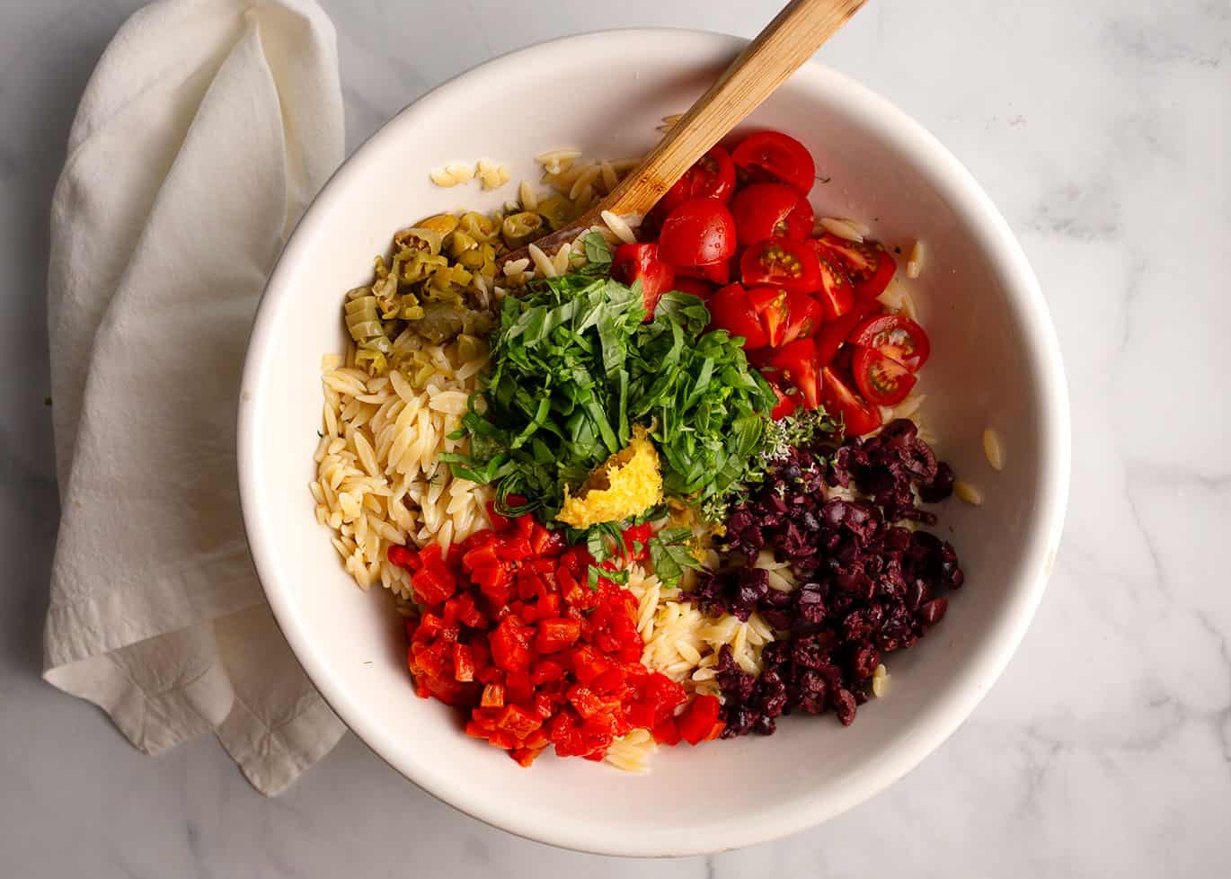 All of the ingredients in the large white bowl with the orzo pasta.