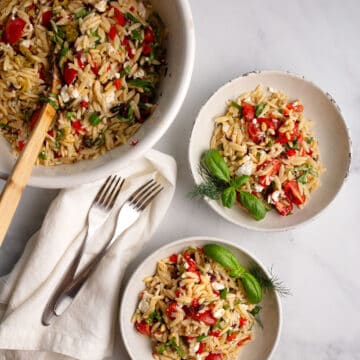 Helpings of Mediterranean Orzo Salad in French pottery bowls, garnished with basil and dill.