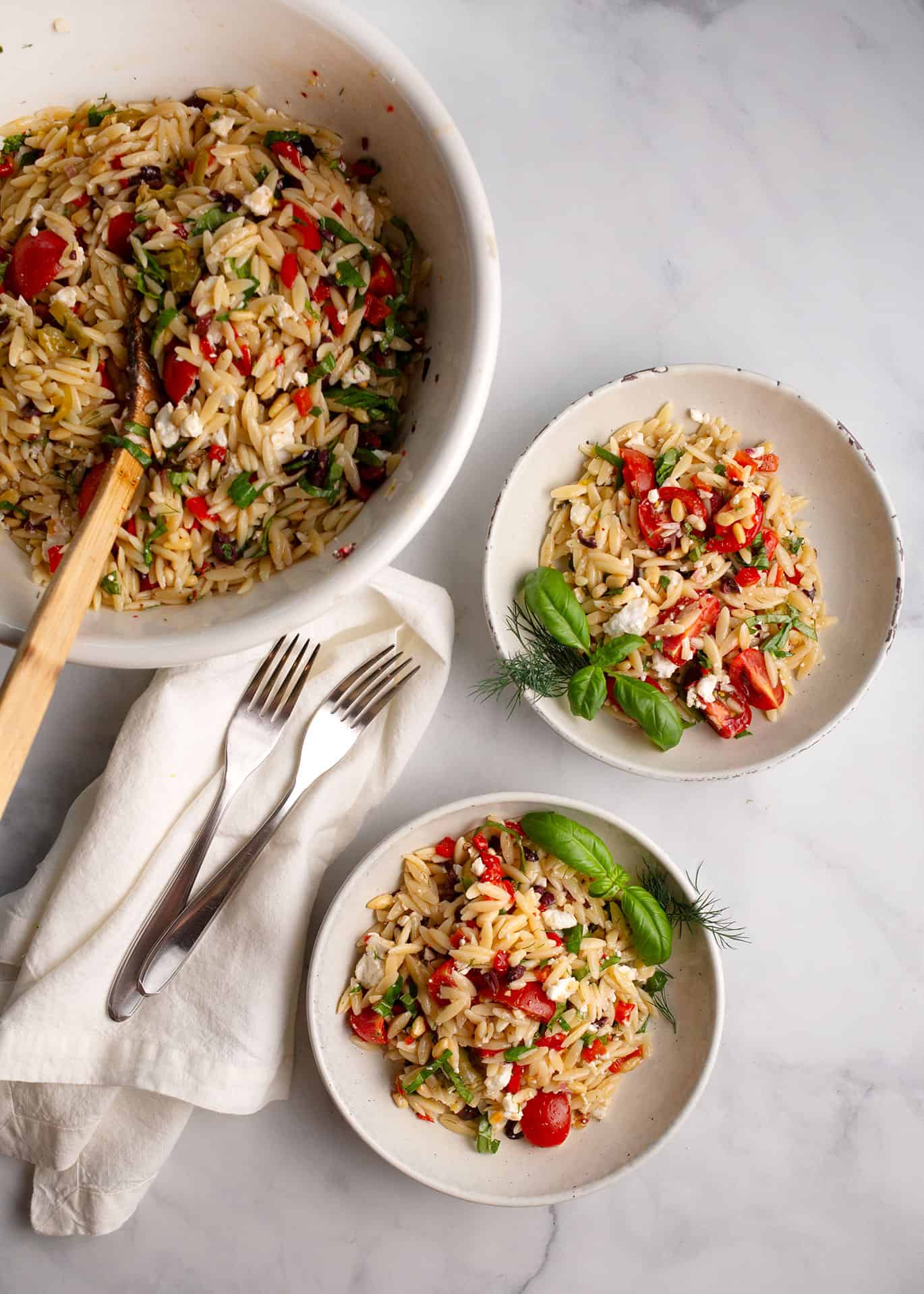 Helpings of Mediterranean Orzo Salad in French pottery bowls, garnished with basil and dill.