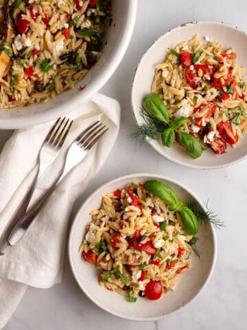 Two servings of Mediterranean Orzo Salad garnished with herbs in pottery bowls