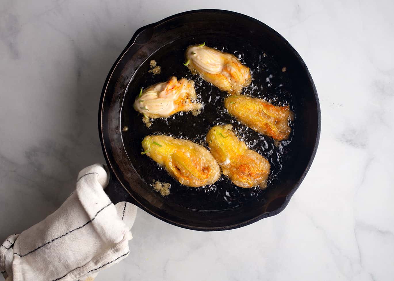 A skillet with a little oil is all it takes to fry the zucchini flowers crispy.