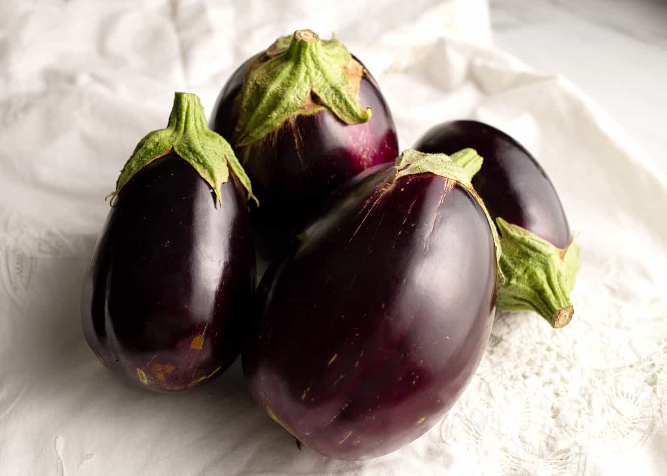 Four eggplants on a Battenburg cloth