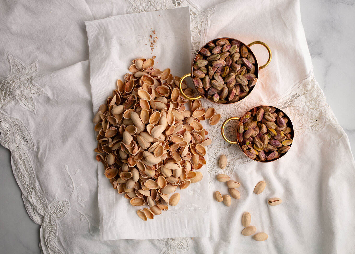 Shelled pistachios in copper cups on Battenburg cloth