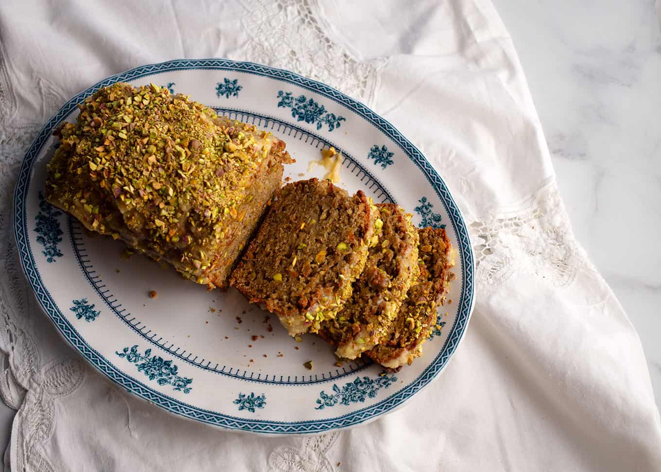 A loaf of Sweet Eggplant & Pistachio Quick Bread sliced on a blue transferware platter.