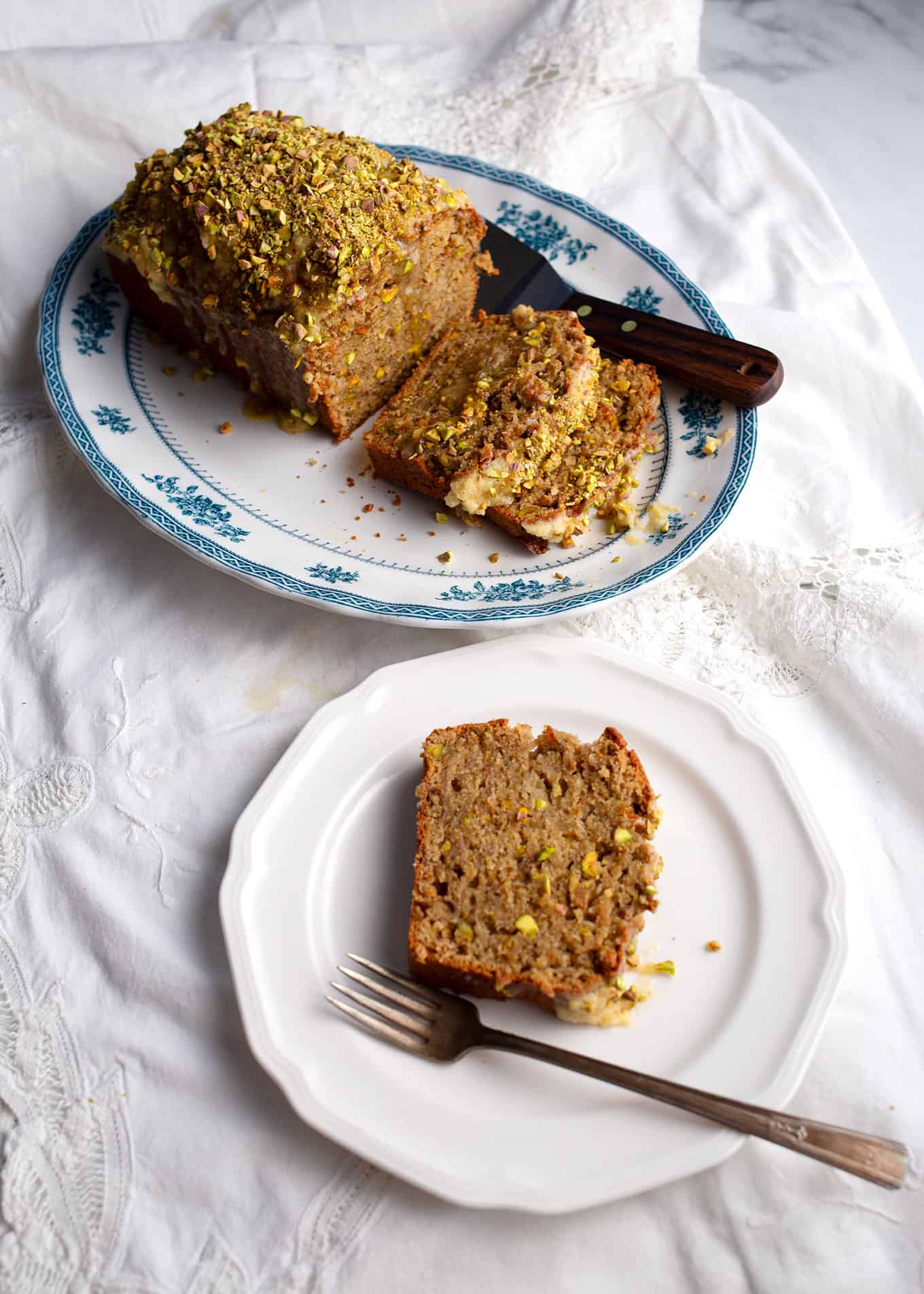 A loaf of bread on a blue transferware platter with a slice on a plate with a fork